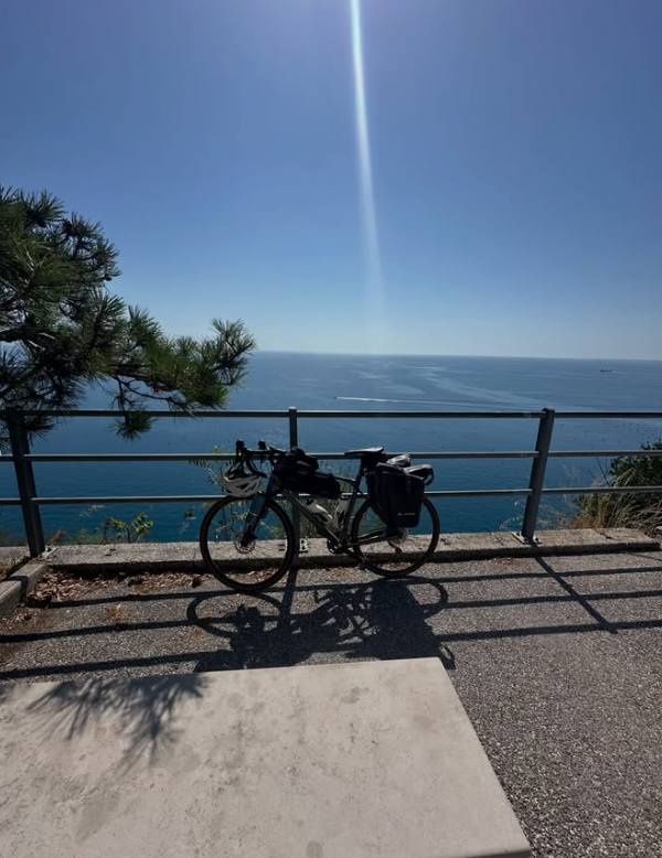 En packad cykel vid räcket, med havet mot Trieste bakom.